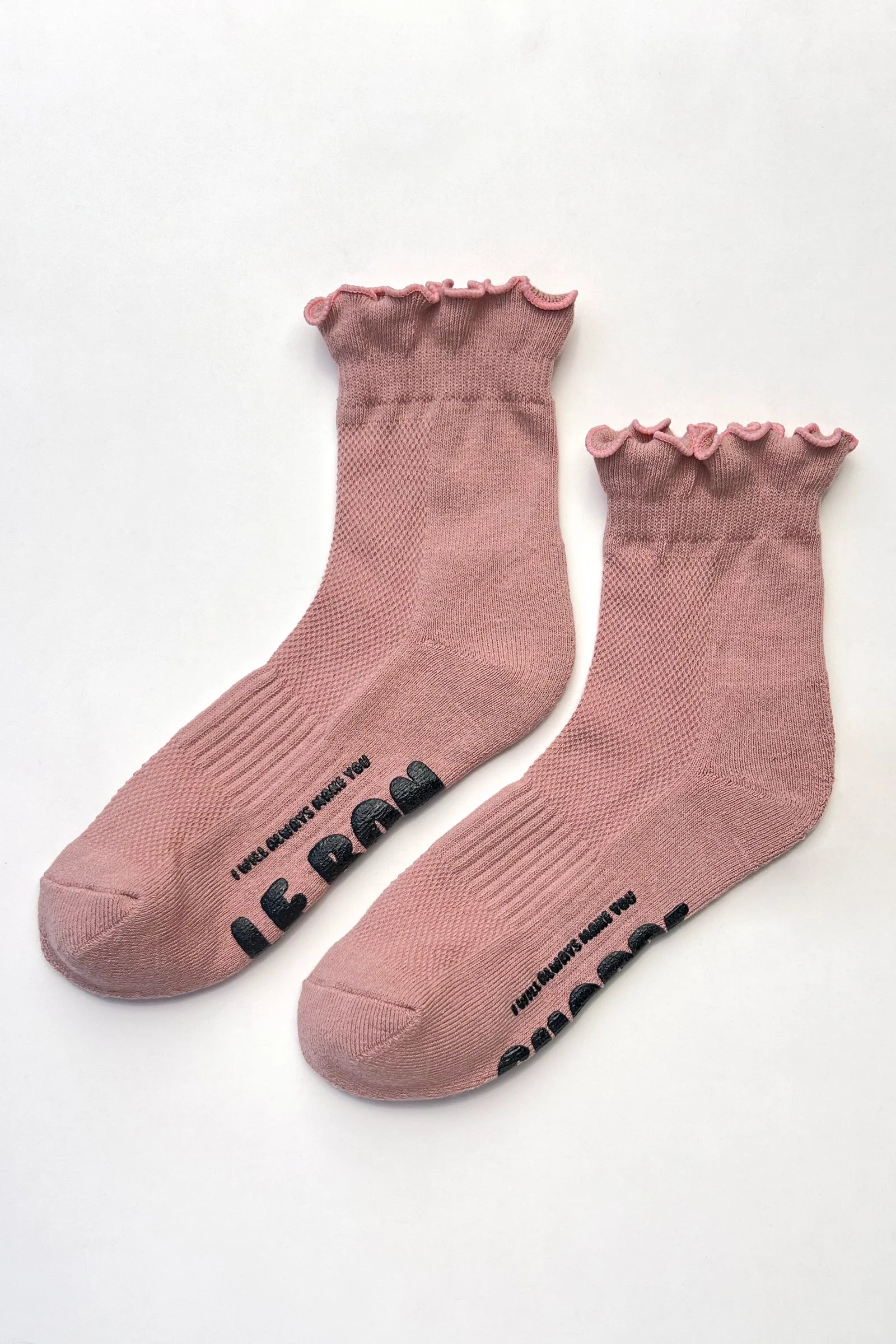 A pair of dusty rose pink ankle socks with ruffled trim at the top and black text printed on the soles, displayed on a clean white background.