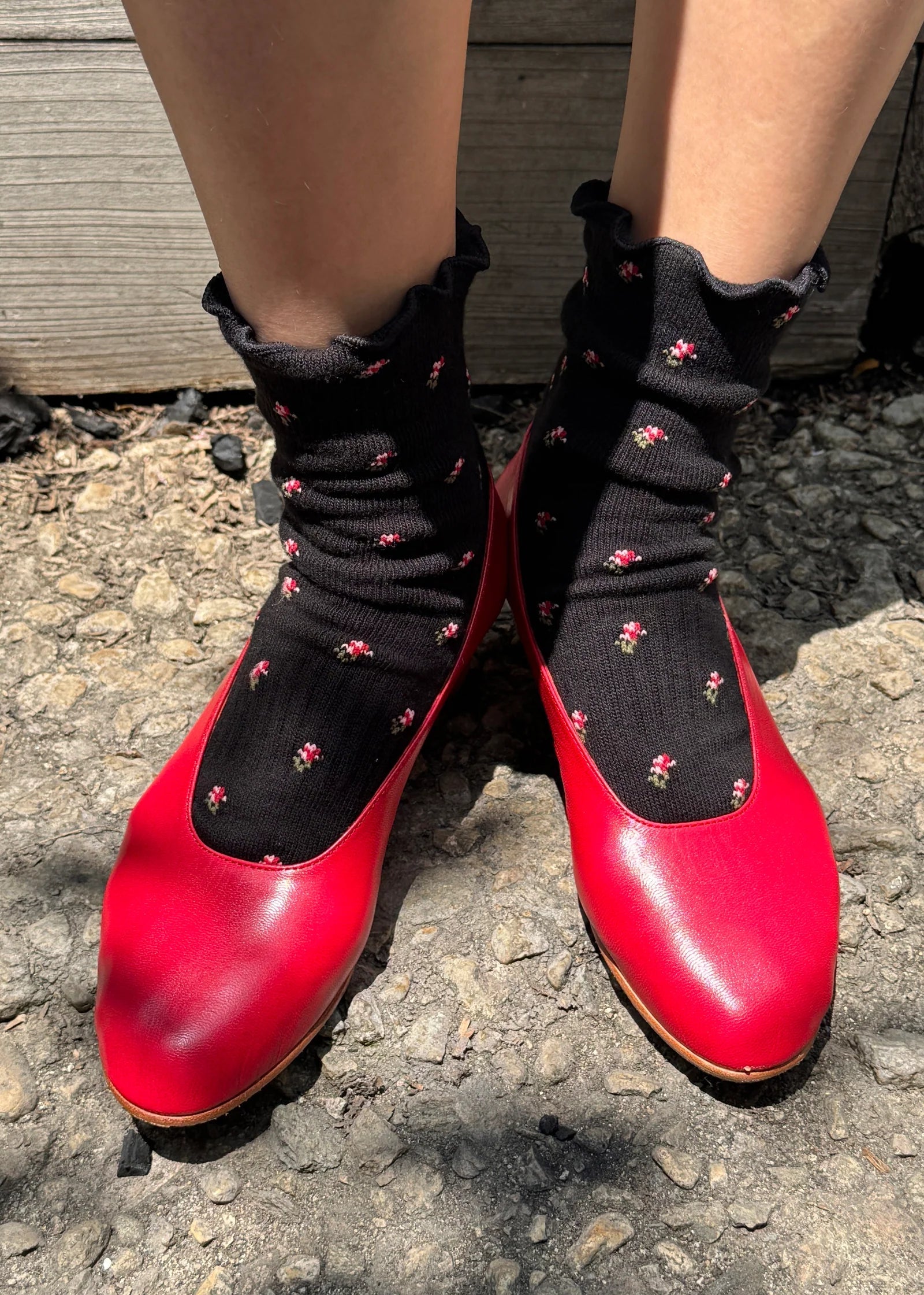 Red shoes with black socks featuring pink flowers on a stone surface.