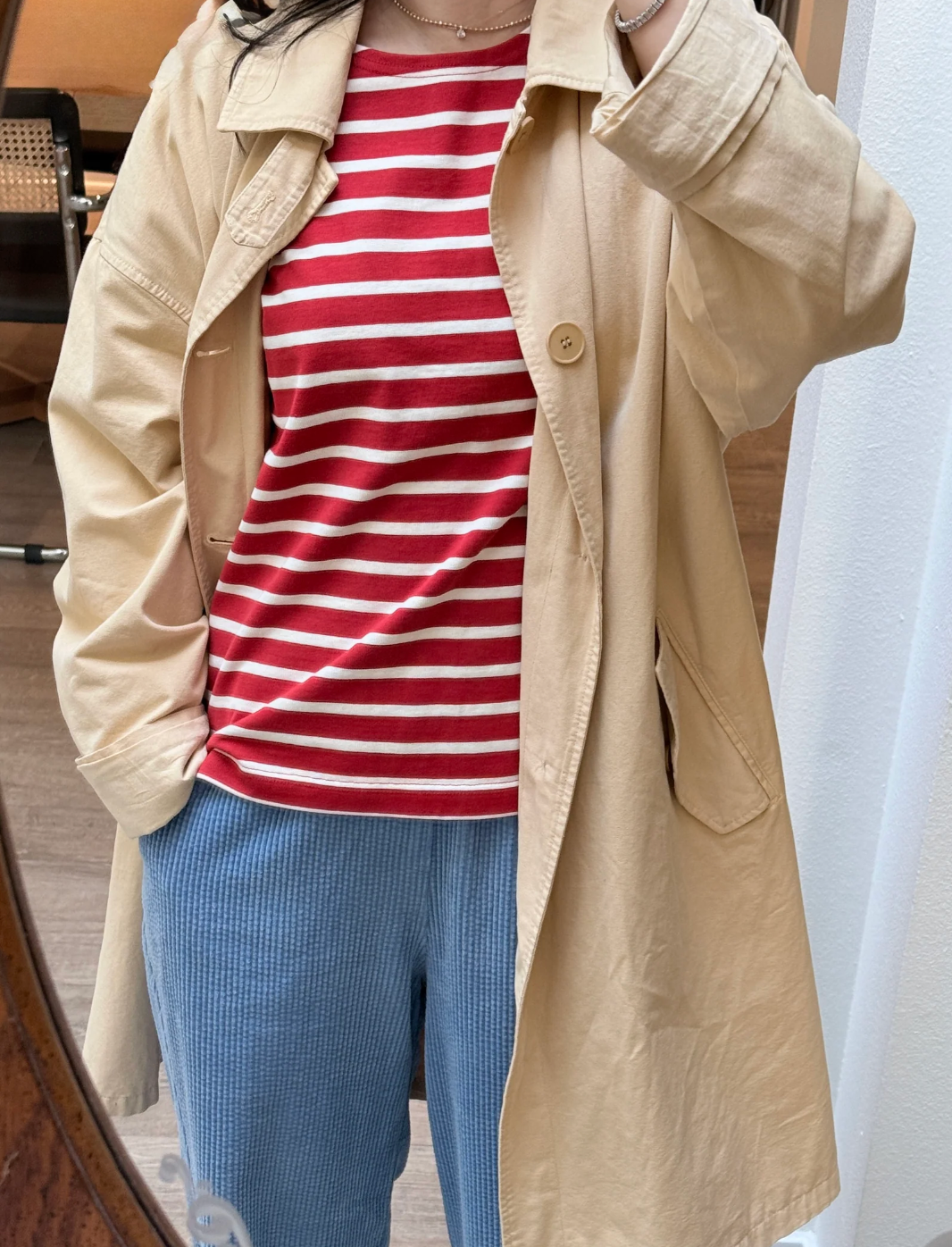 Person wearing a beige trench coat over a red and white striped shirt and blue pants.