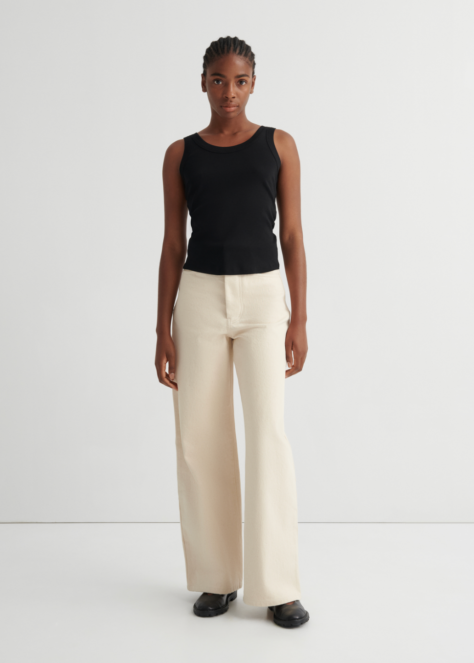 Person wearing a black sleeveless top and beige pants on a white background
