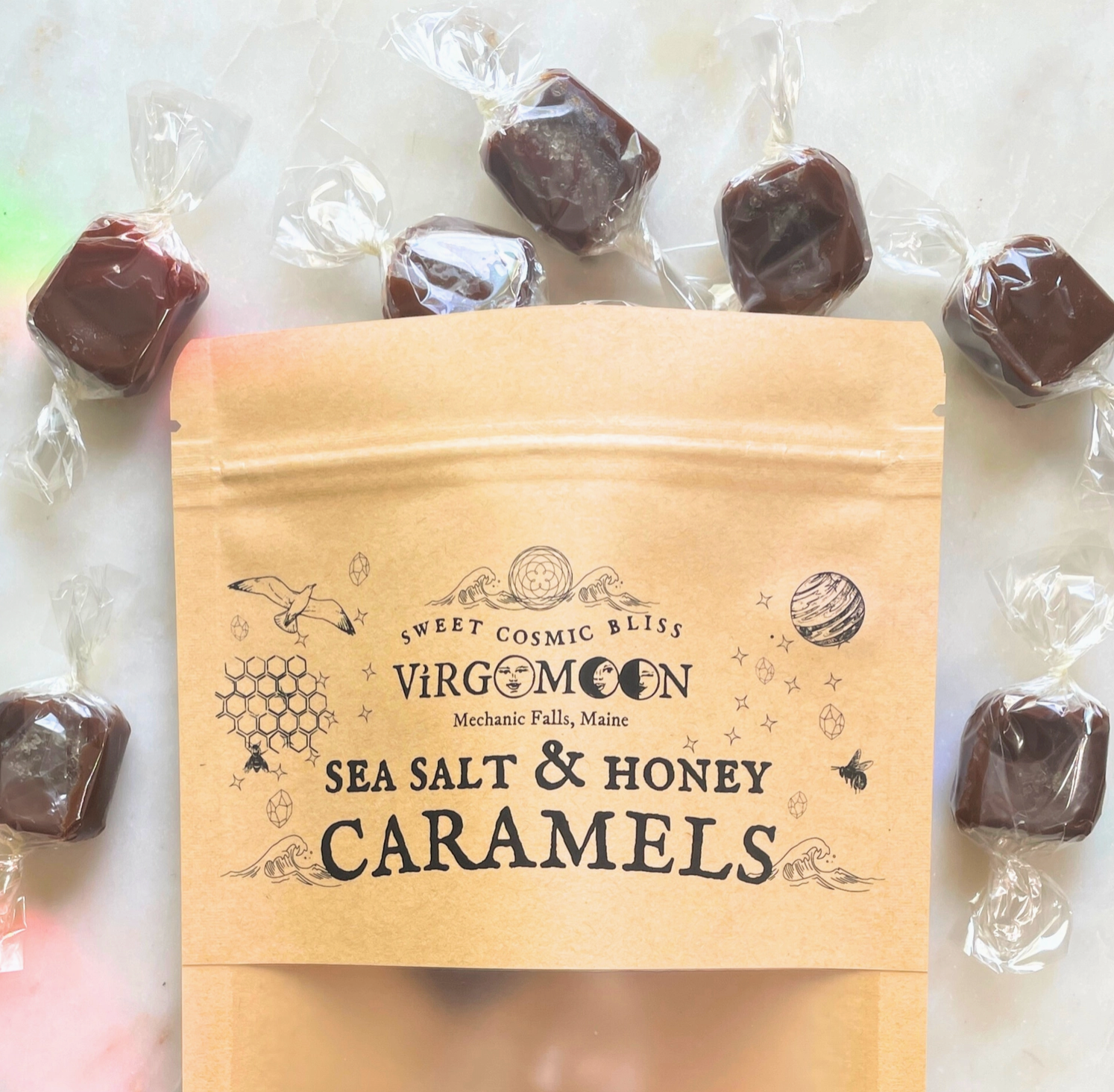 Bag of Virgo Moon sea salt & honey caramels surrounded by individually wrapped caramels on a light background