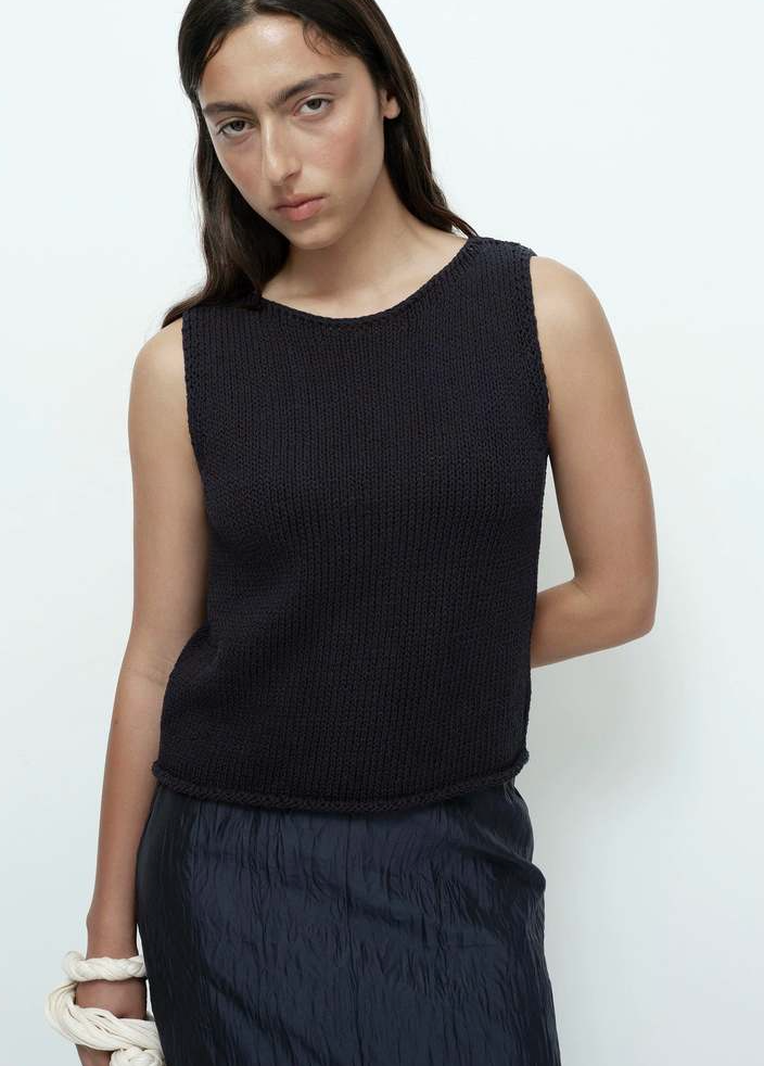 woman wearing black knit sleeveless top and navy crinkled skirt
