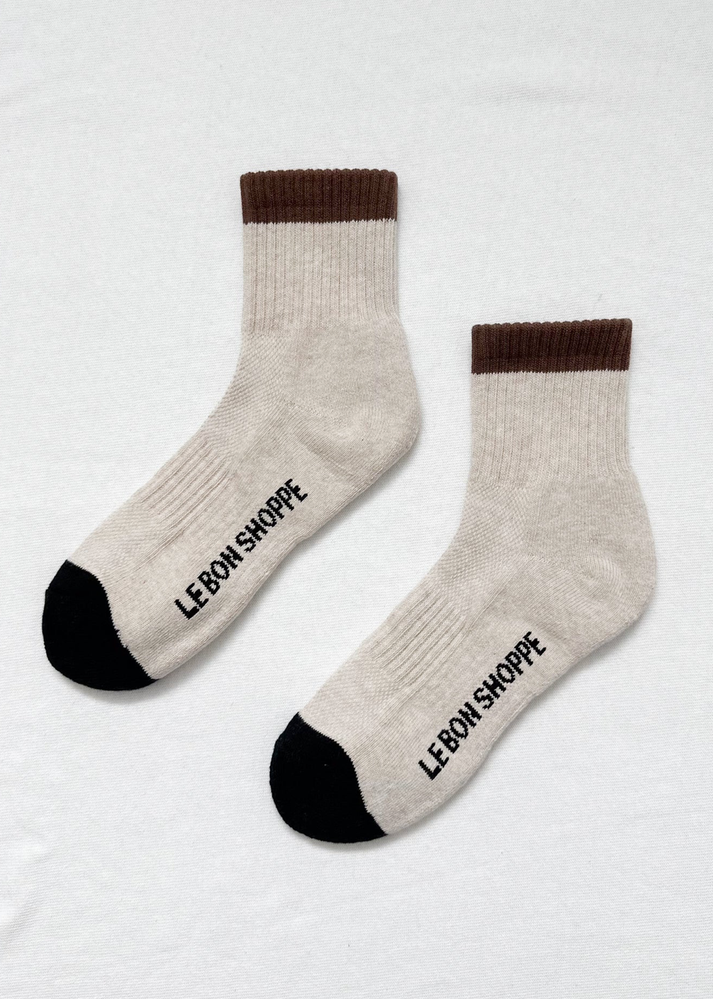 Pair of beige socks with brown and black accents on a light gray background