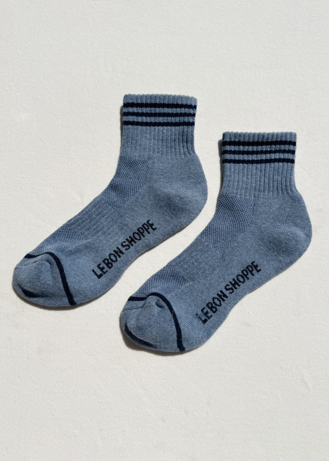 Pair of blue socks with black stripes and 'Le Bon Shoppe' branding on a light gray background