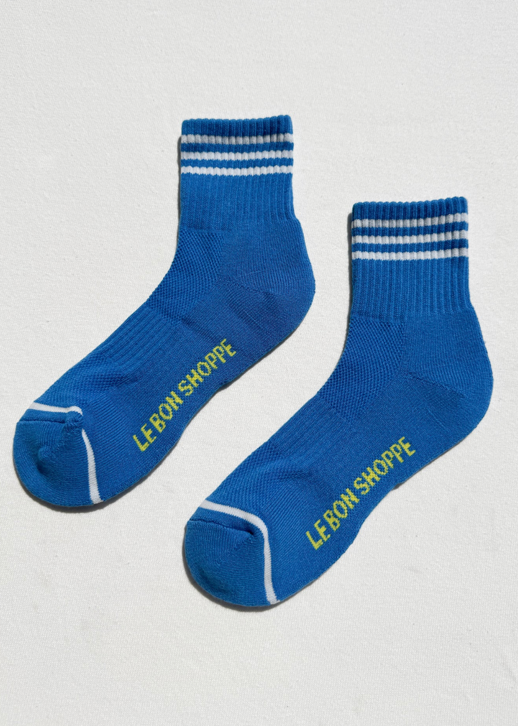 Blue socks with white stripes and 'Le Bon Shoppe' branding on a light gray background