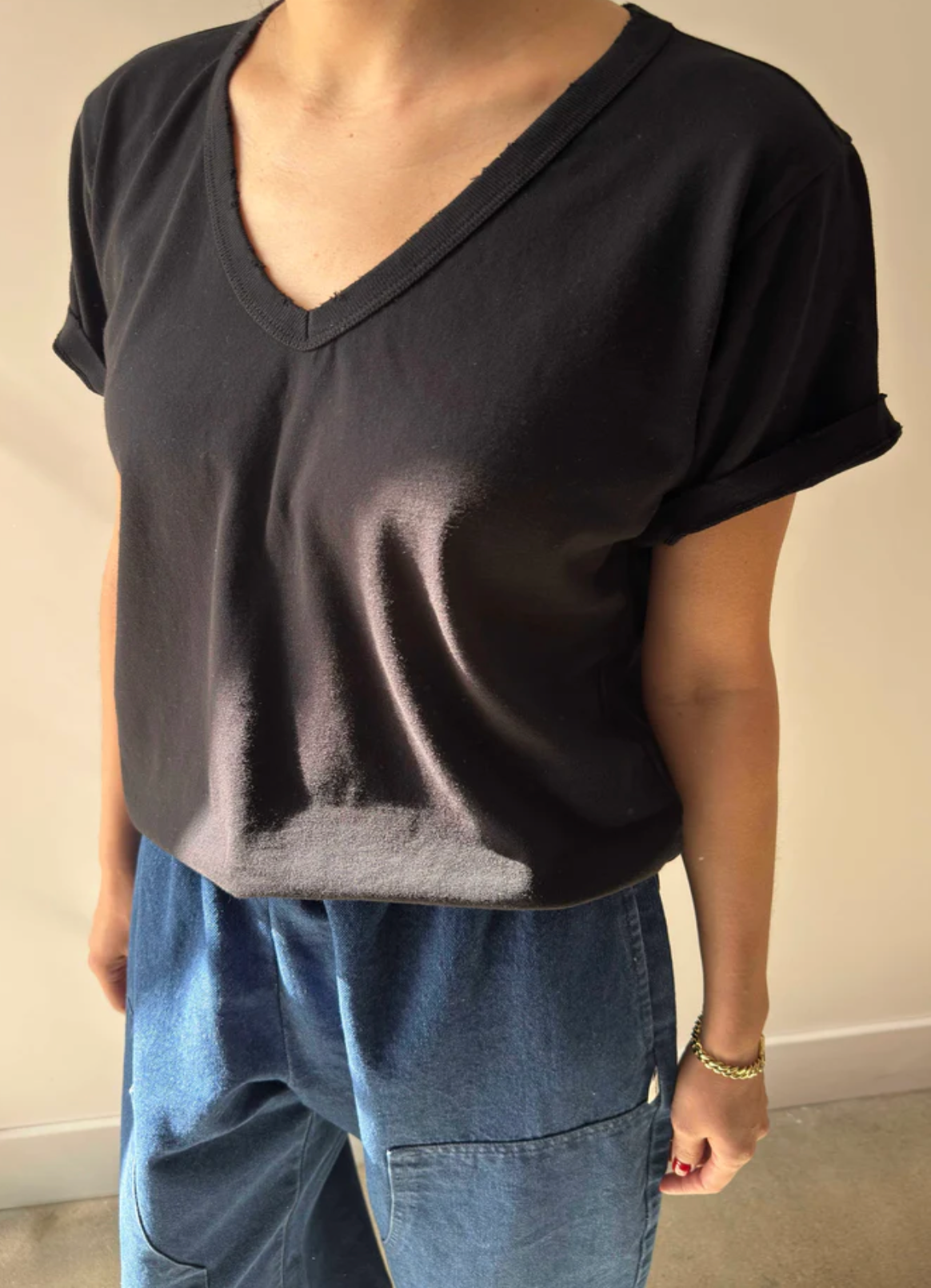 Person wearing a black V-neck t-shirt and blue jeans against a plain background