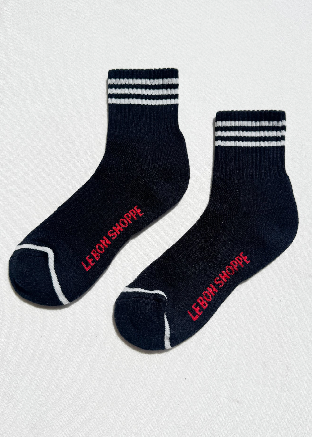 Pair of black socks with white stripes and red text on a light gray background