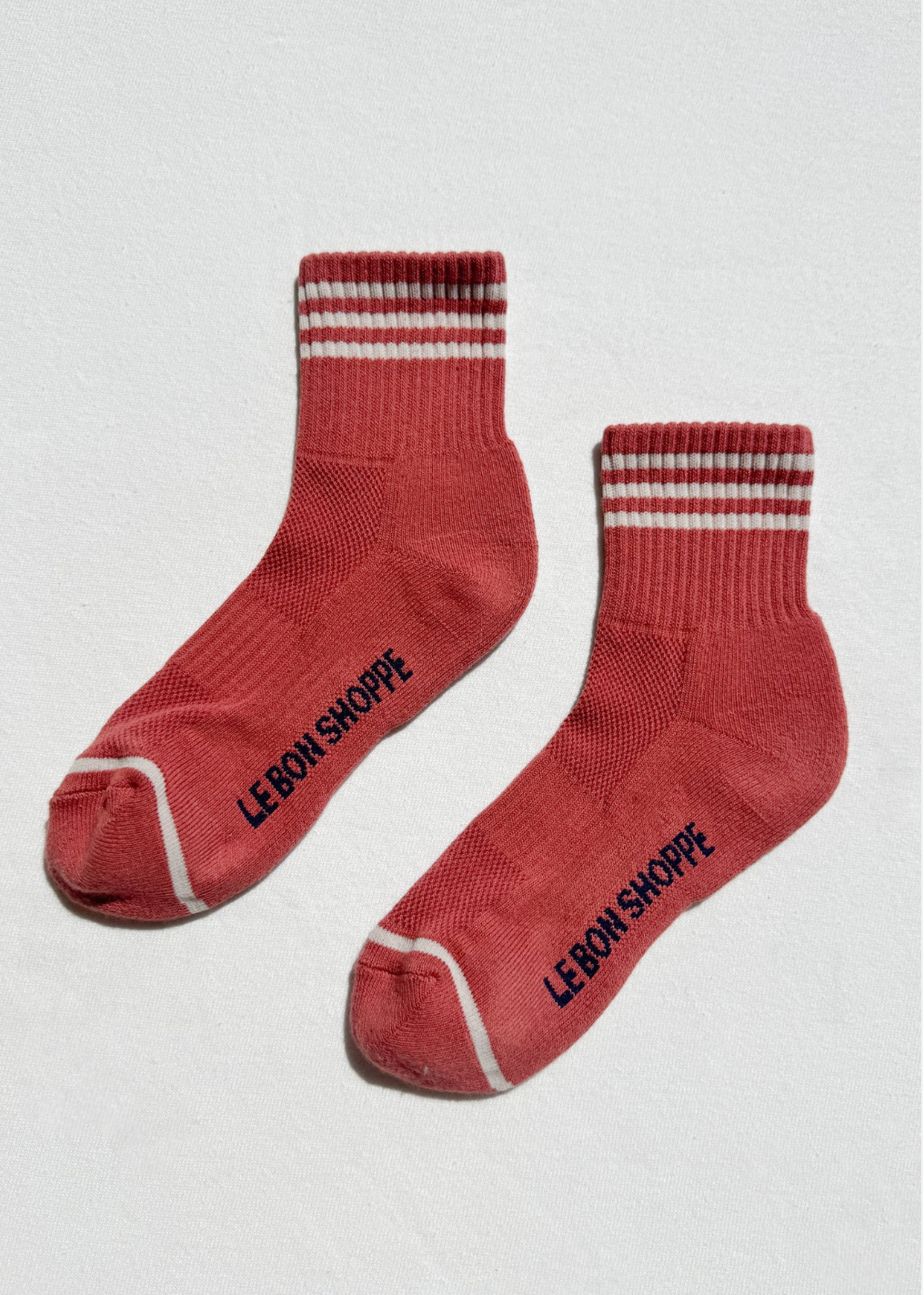 Red orange socks with white stripes and branding on a light gray background