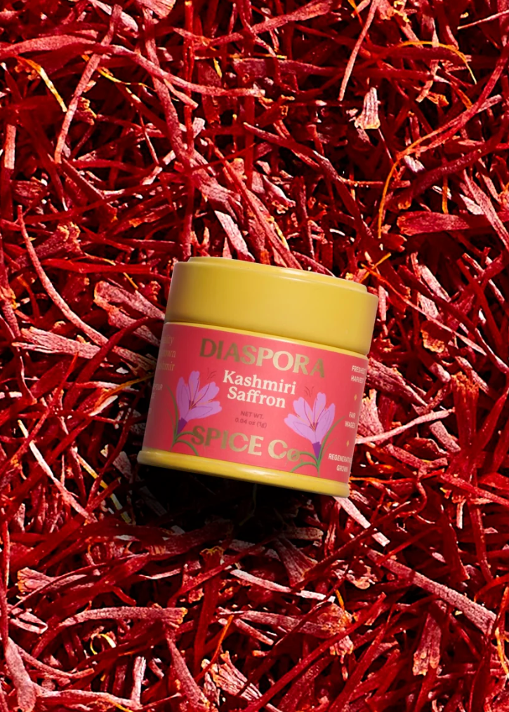 A small jar of Diaspore Kashmiri Saffron resting on a bed of dried red saffron threads. The jar has a yellow lid and a pink label with white text.
