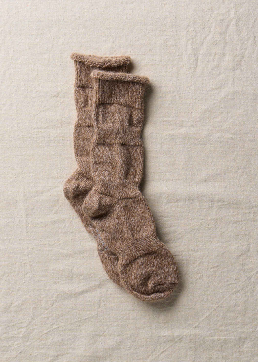 A single pair of thick, ribbed knit socks in a warm taupe-brown color, laid flat on a textured off-white fabric background.