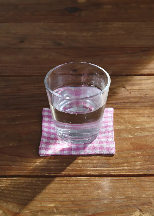 water on a pink and white fabric gingham coaster on a wooden table
