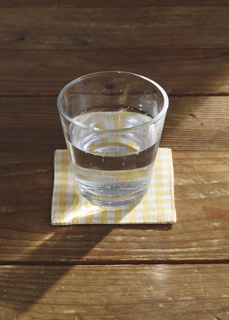 glass of water on a yellow and white gingham coaster on a wooden table 