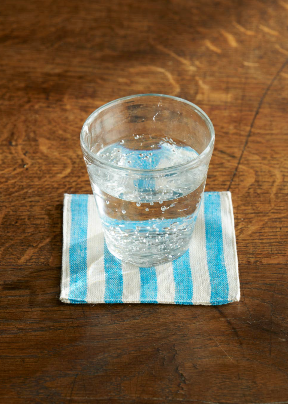glass of water on a cloth white and blue striped coaster on a wooden table