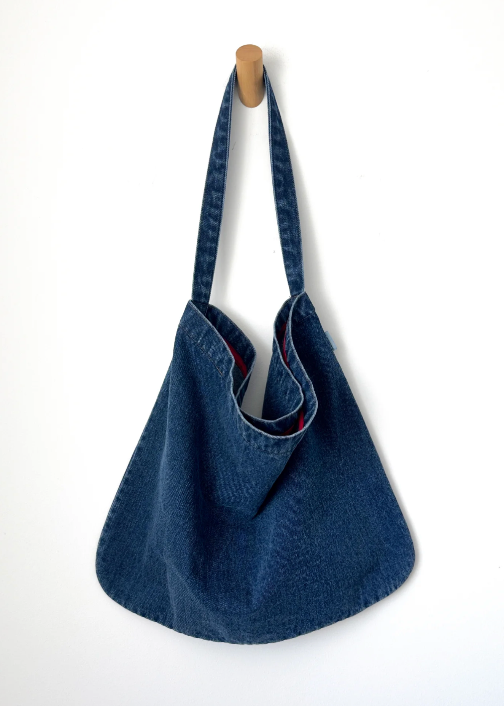 Blue denim bag hanging on a wooden hook against a white background