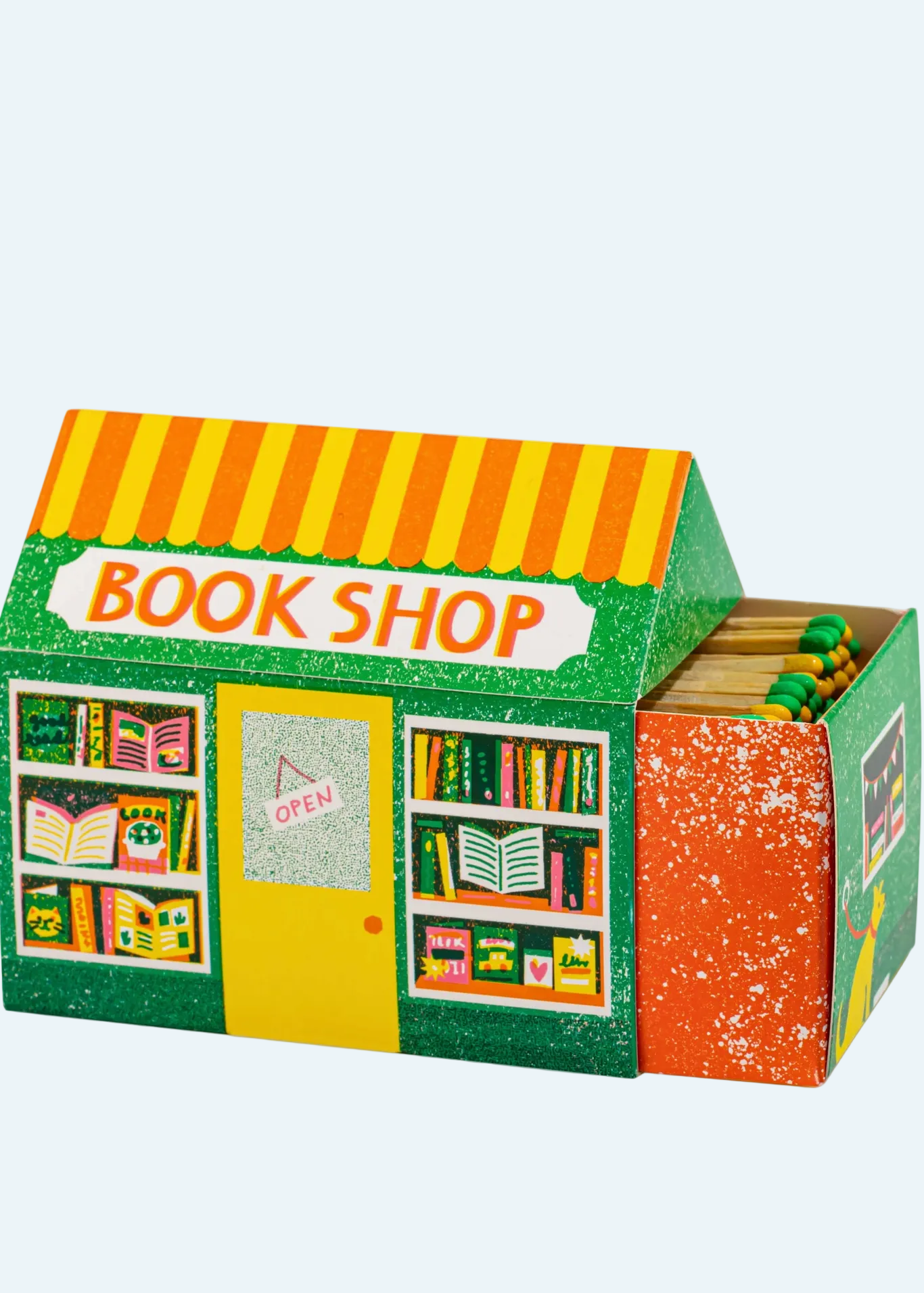 A children's toy bookshop box with a green and yellow striped awning, colorful bookshelves filled with miniature books, a yellow front door with an 'OPEN' sign, and a side compartment with orange and green details.