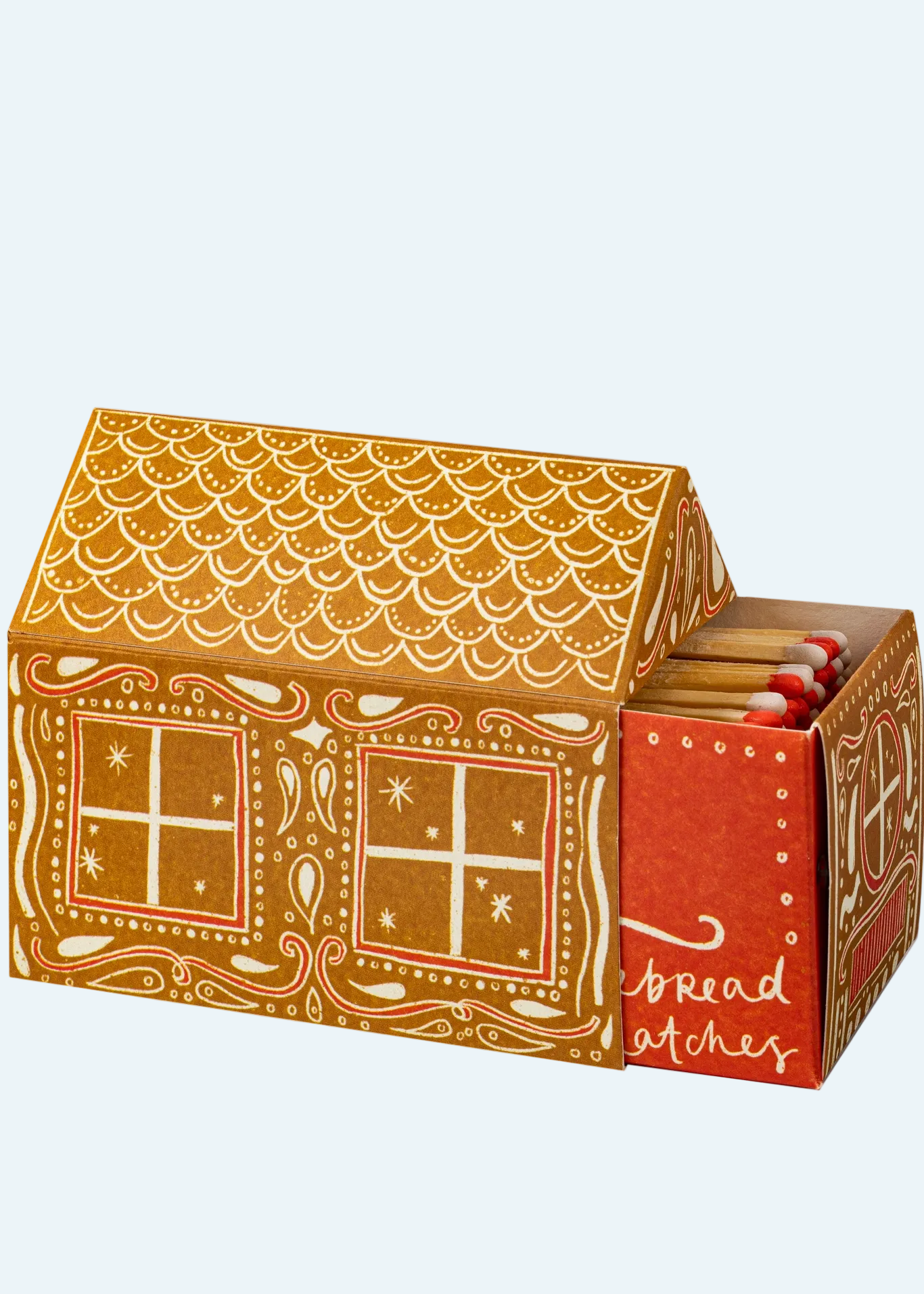 A gingerbread-themed matchbox box with a house design, shown open to reveal red match sleeves inside. The box is decorated with white icing-style patterns and the words 'bread patches' on the front.