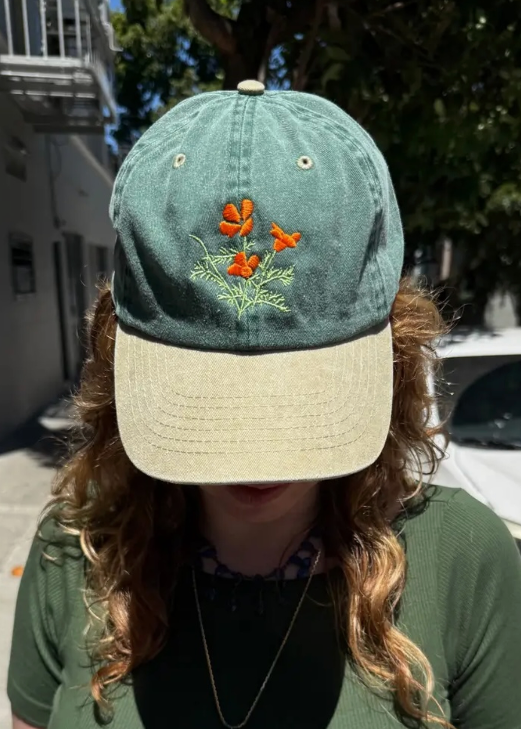 two tone hat with green on top and tan bill with an orange poppy flower design in the middle of the front (on a model)