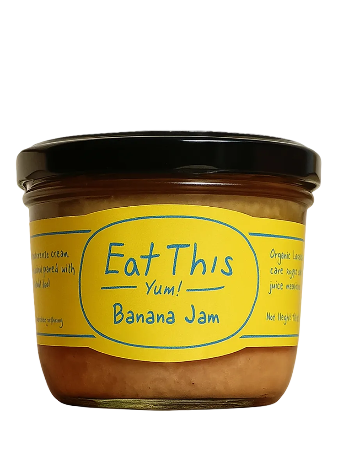 A glass jar of banana jam with a black lid and a bright yellow label reading 'Eat This Yum! Banana Jam', photographed on a light surface with a softly blurred background.