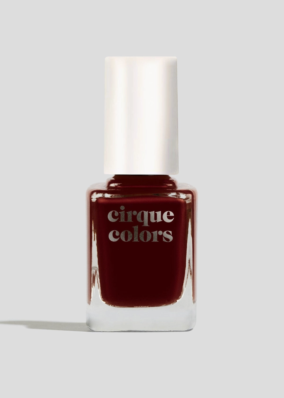 A bottle of Cirque Colors nail polish in a deep burgundy red shade, featuring a white cylindrical cap and a clear glass base, set against a solid light gray background.