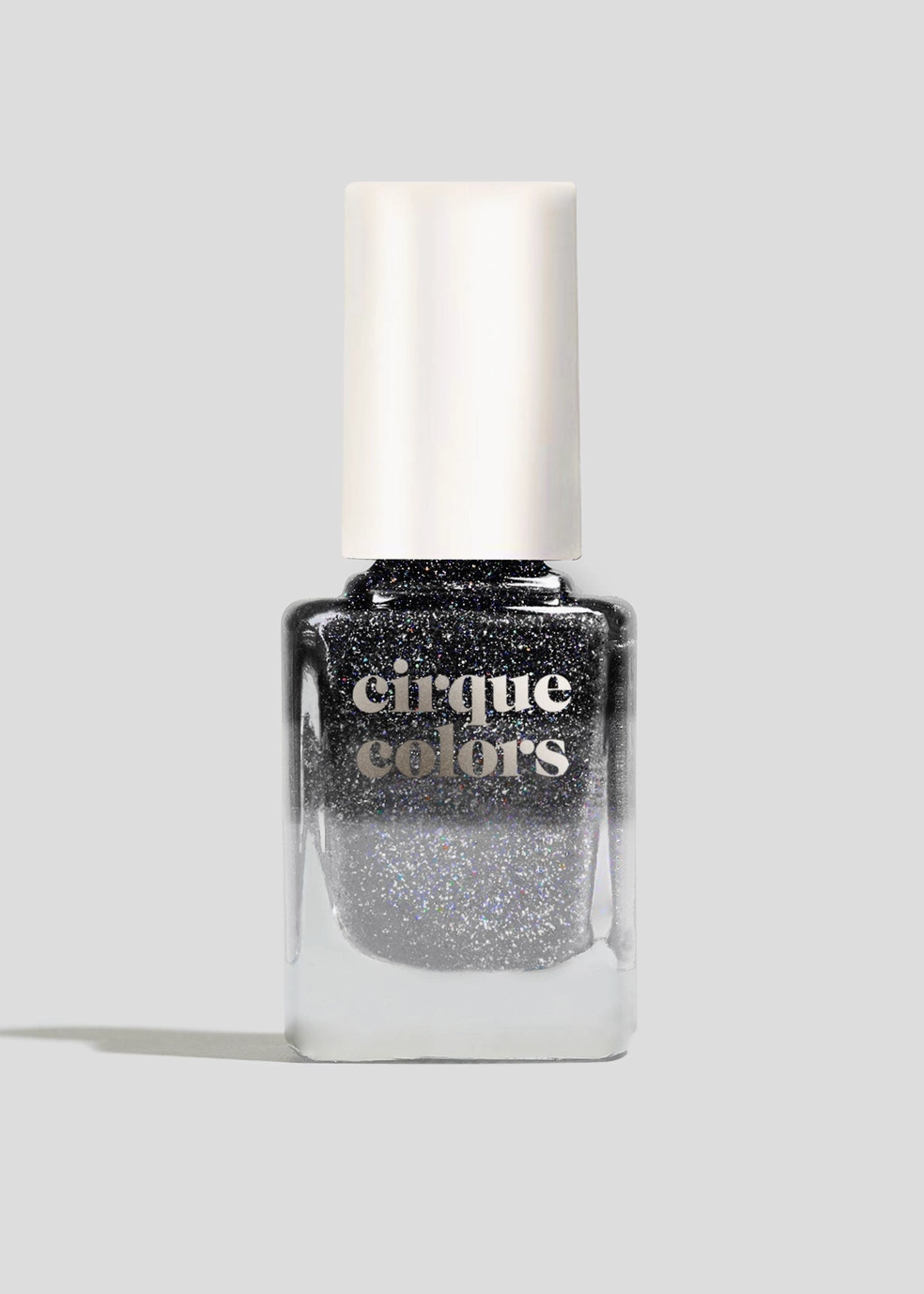 A bottle of Cirque Colors glitter nail polish in a shimmering silver shade, featuring a white cylindrical cap and a clear glass bottle, set against a solid light gray background.