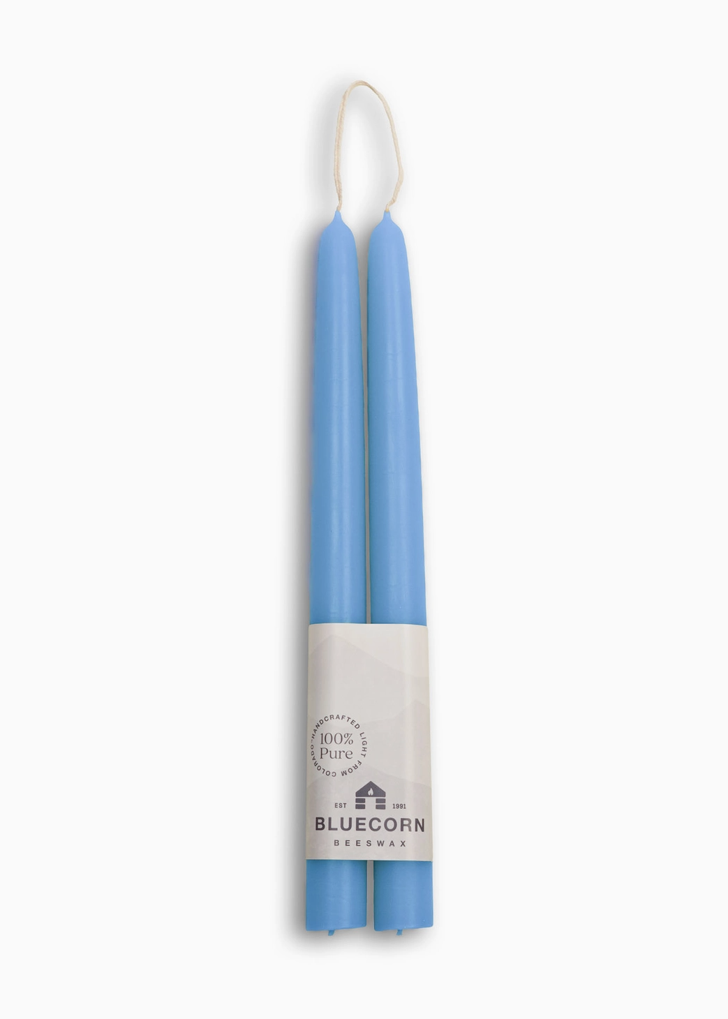 Two light blue taper candles wrapped in a white paper band labeled 'BLUECORN CANDLE CO.' with a small hanging loop at the top, shown on a clean white background.