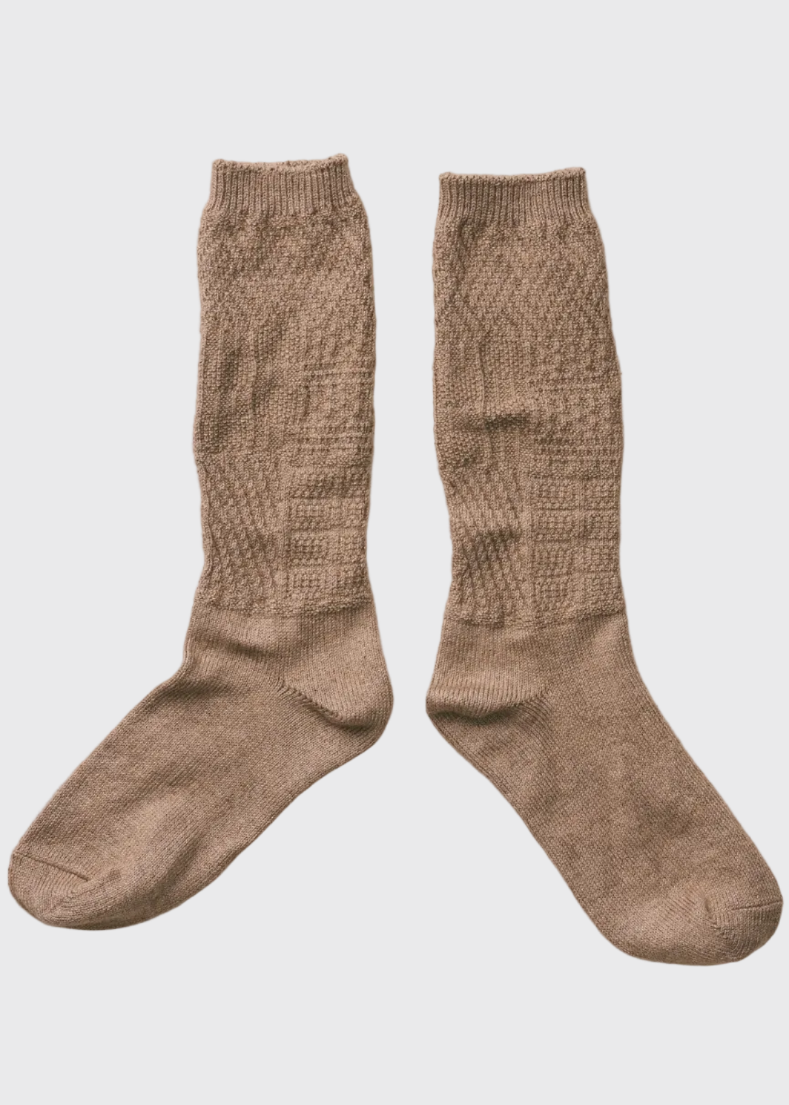 A pair of knee-high knit socks in a warm taupe-brown color, laid flat on a textured off-white fabric background.
