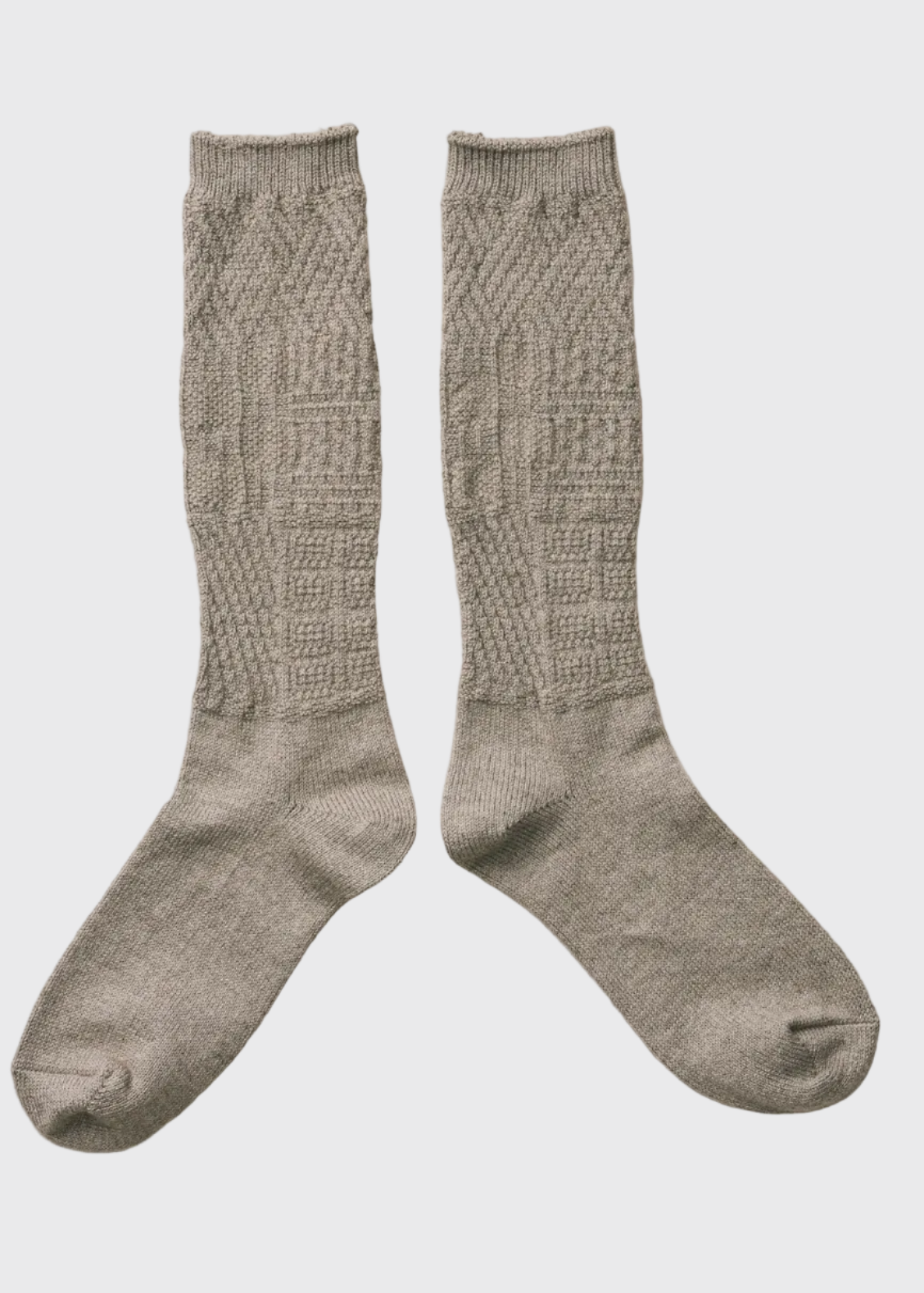 A pair of hand-knit knee-high socks in a heathered taupe-gray color, featuring a textured cable-knit pattern on the leg and a smoother knit lower section, laid flat on a wrinkled off-white fabric background.