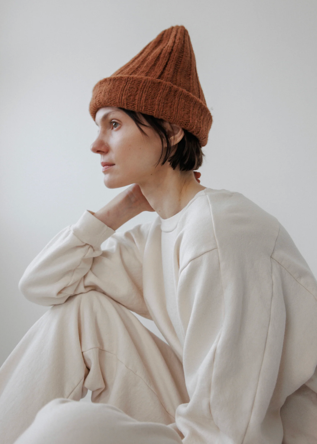 person in white wearing a pointy alpaca hat in a rust color 