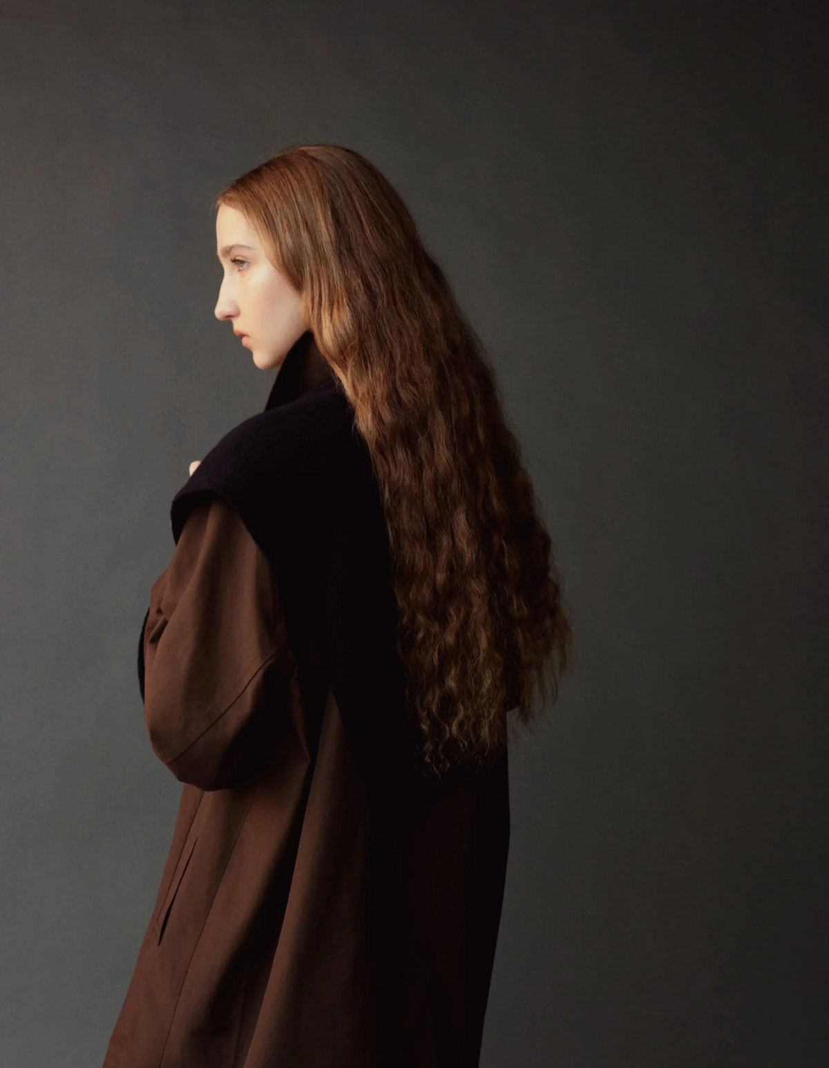 back view of model with long red hair wearing dark shawl and brown trench