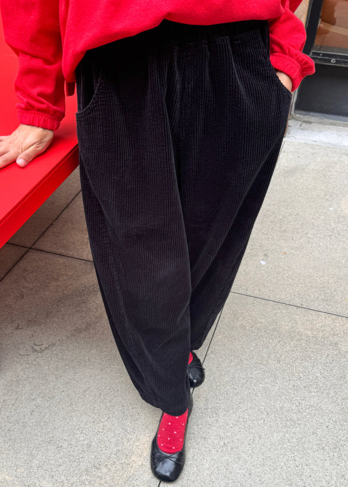 model wearing black cords with red socks and black ballet flats and red sweater.