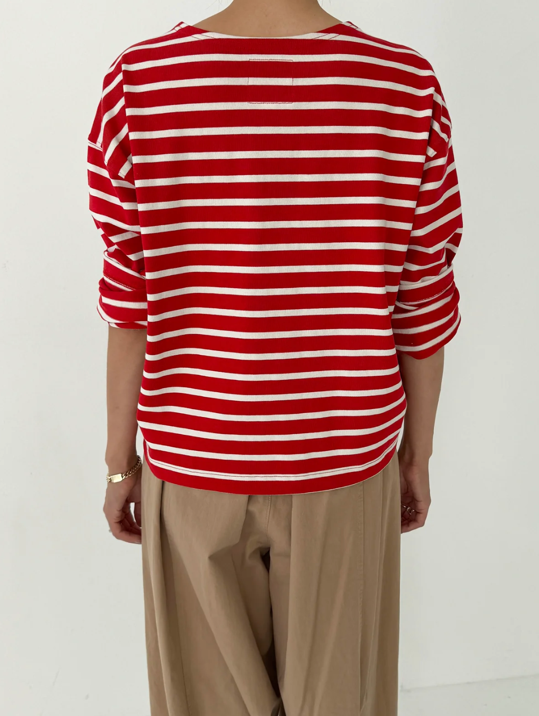 Person wearing a red and white striped shirt with beige pants on a white background