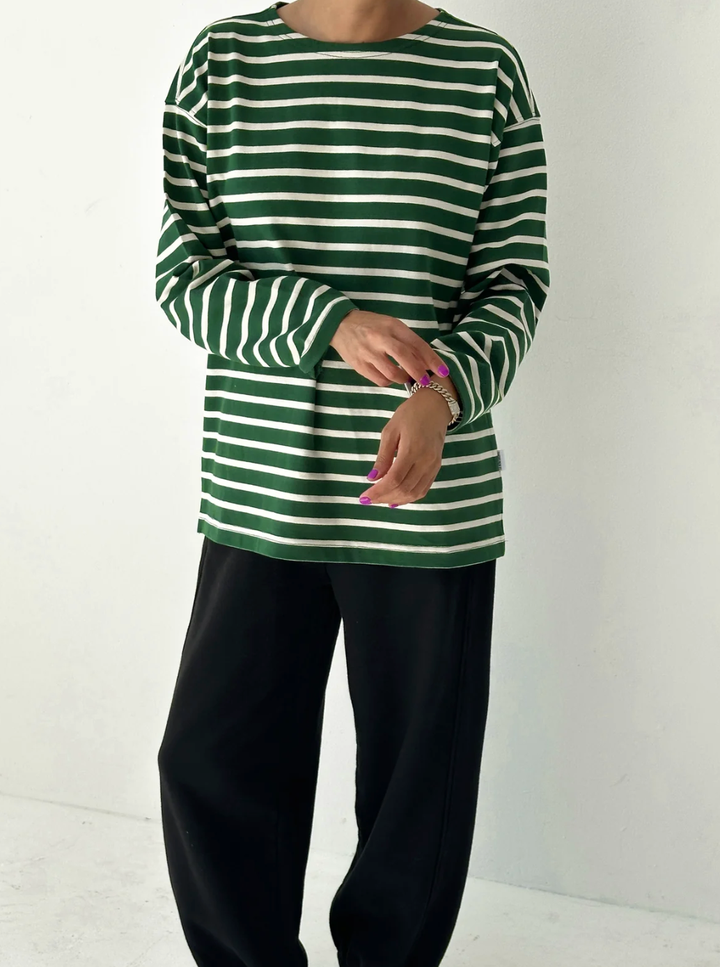 Green and white striped long-sleeve top worn by a person on a white background