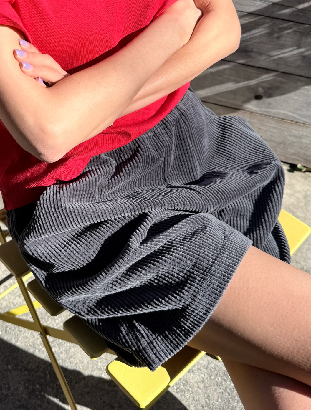 Person wearing a red shirt and gray shorts sitting on a yellow chair.