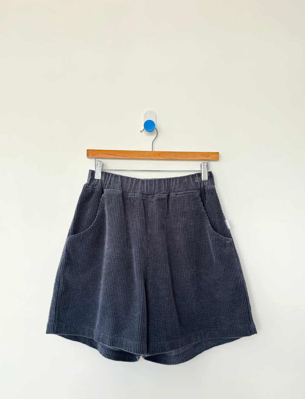 Blue corduroy shorts on a hanger against a white background