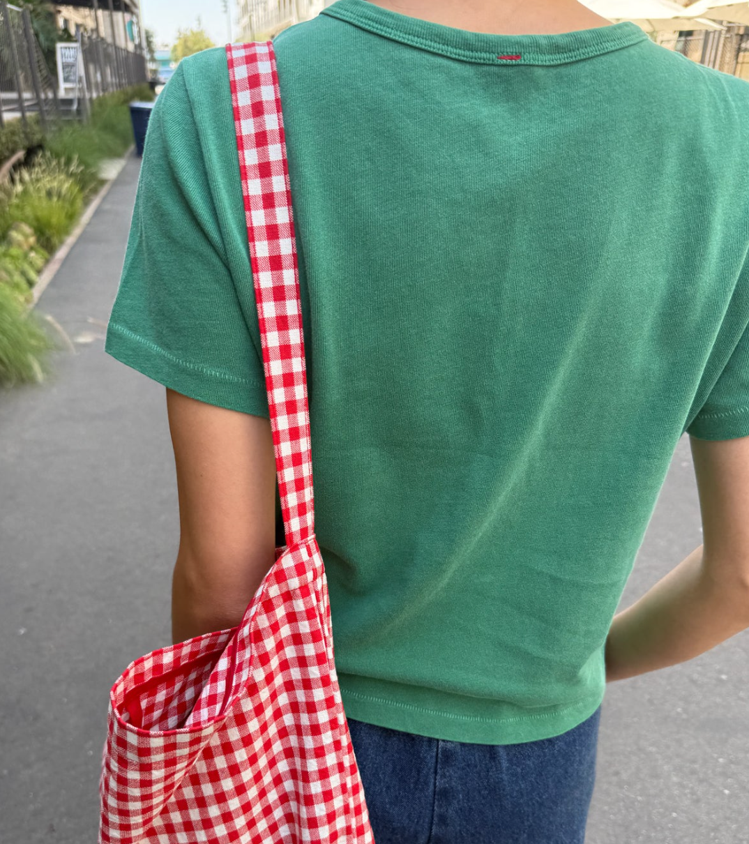 Person wearing a green shirt with a red and white checkered bag over one shoulder.