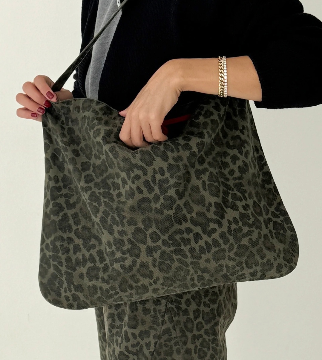 Person holding a green leopard print bag against a neutral background