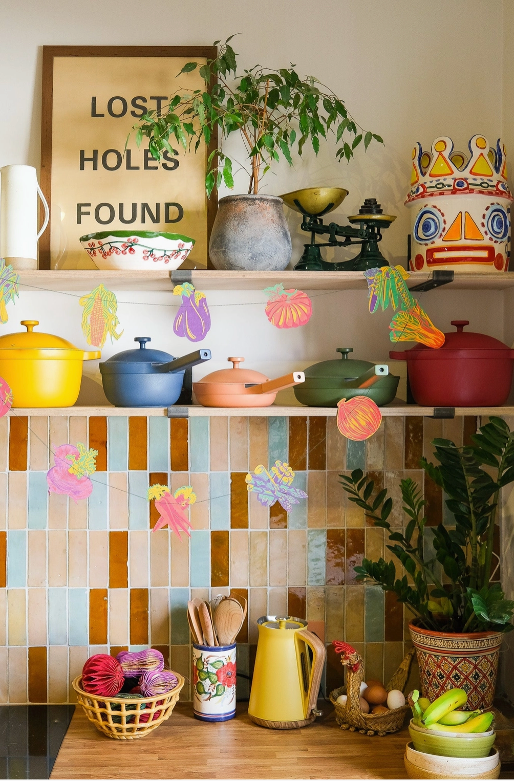 Colorful kitchen scene with pots, pans, and decorative items on shelves against a tiled wall.