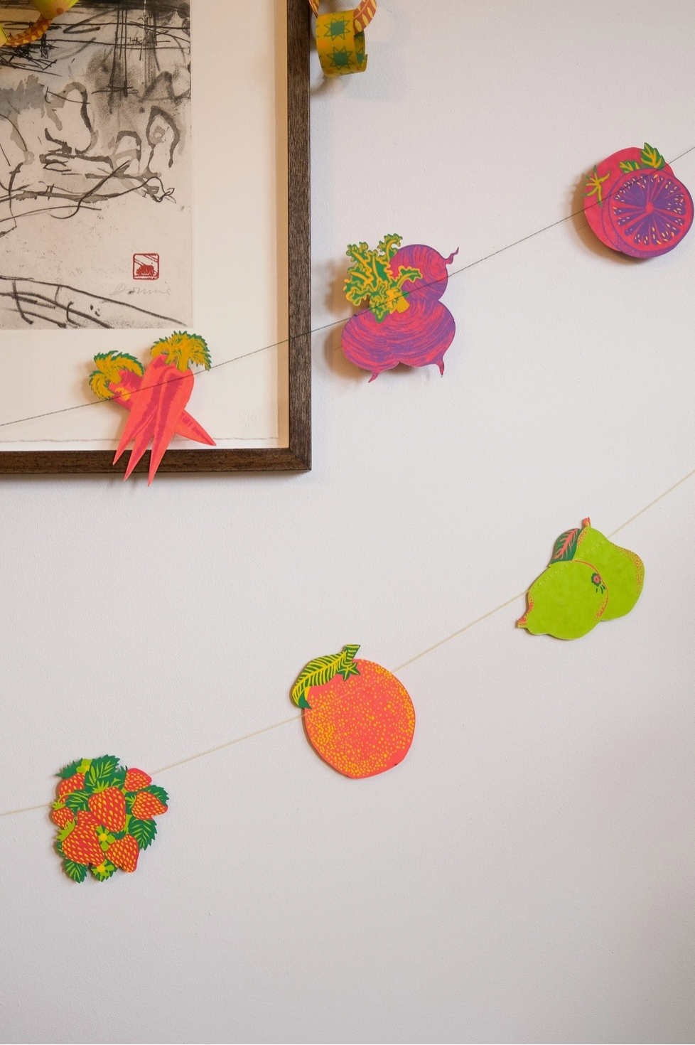 Decorative fruit-themed garland on a white wall with a framed picture.