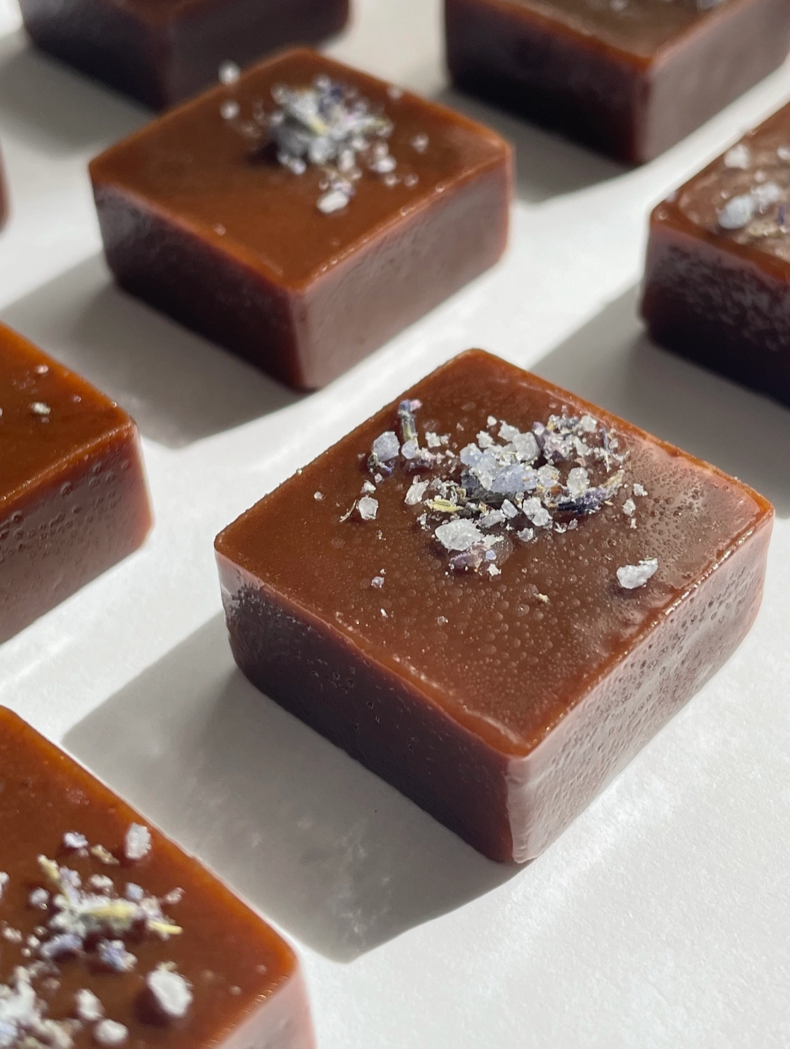 Square caramel candies with lavender sea salt on a white surface