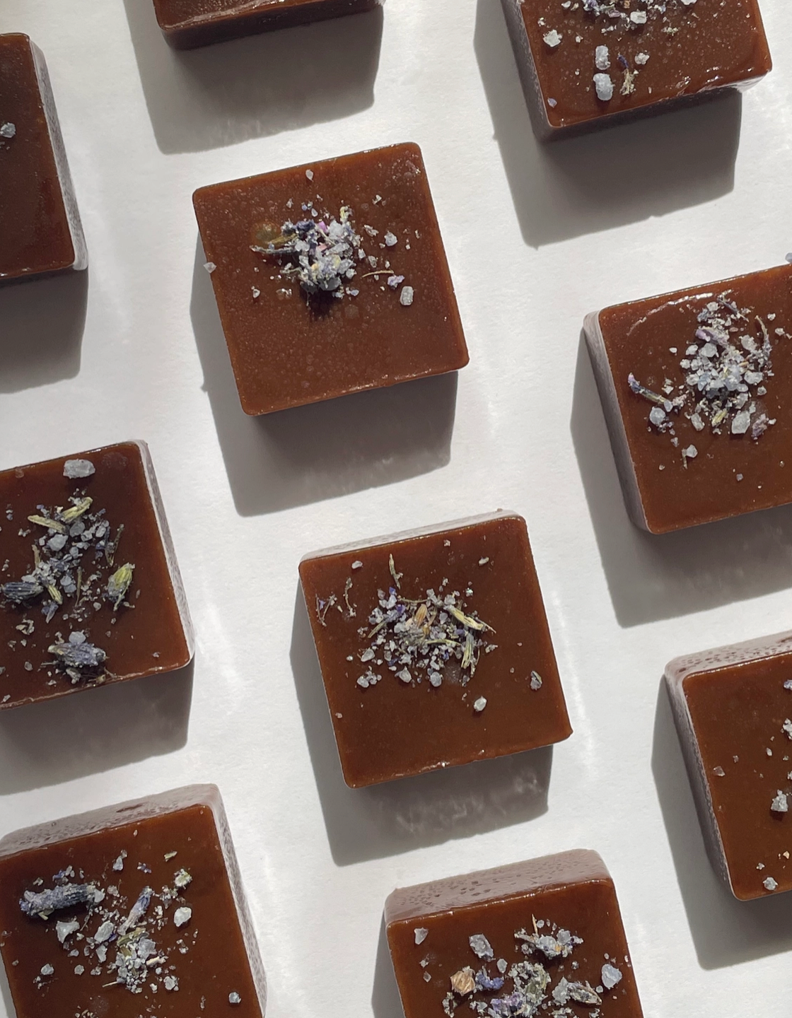 Square caramel candies with lavender sea salt on a white surface