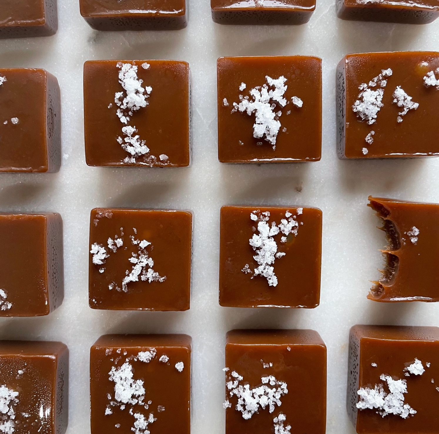 Square caramel candies with white flake salt arranged in a grid on a light background.