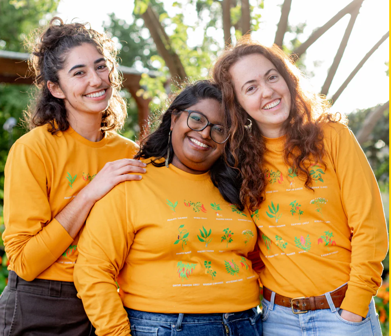 Three people wearing matching yellow sweaters with a plant pattern outdoors.