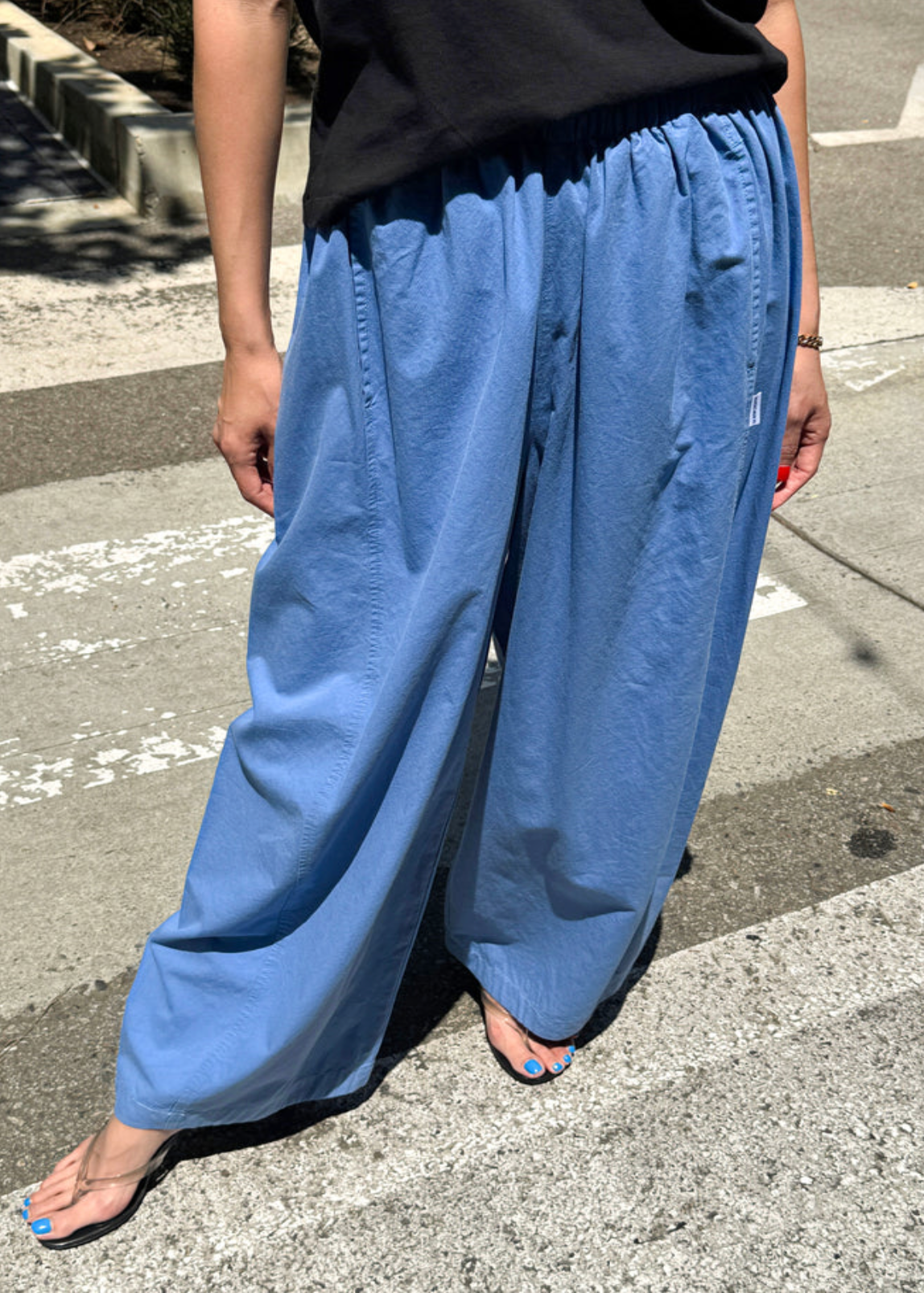 Person wearing blue wide-leg pants and a black top on a street.