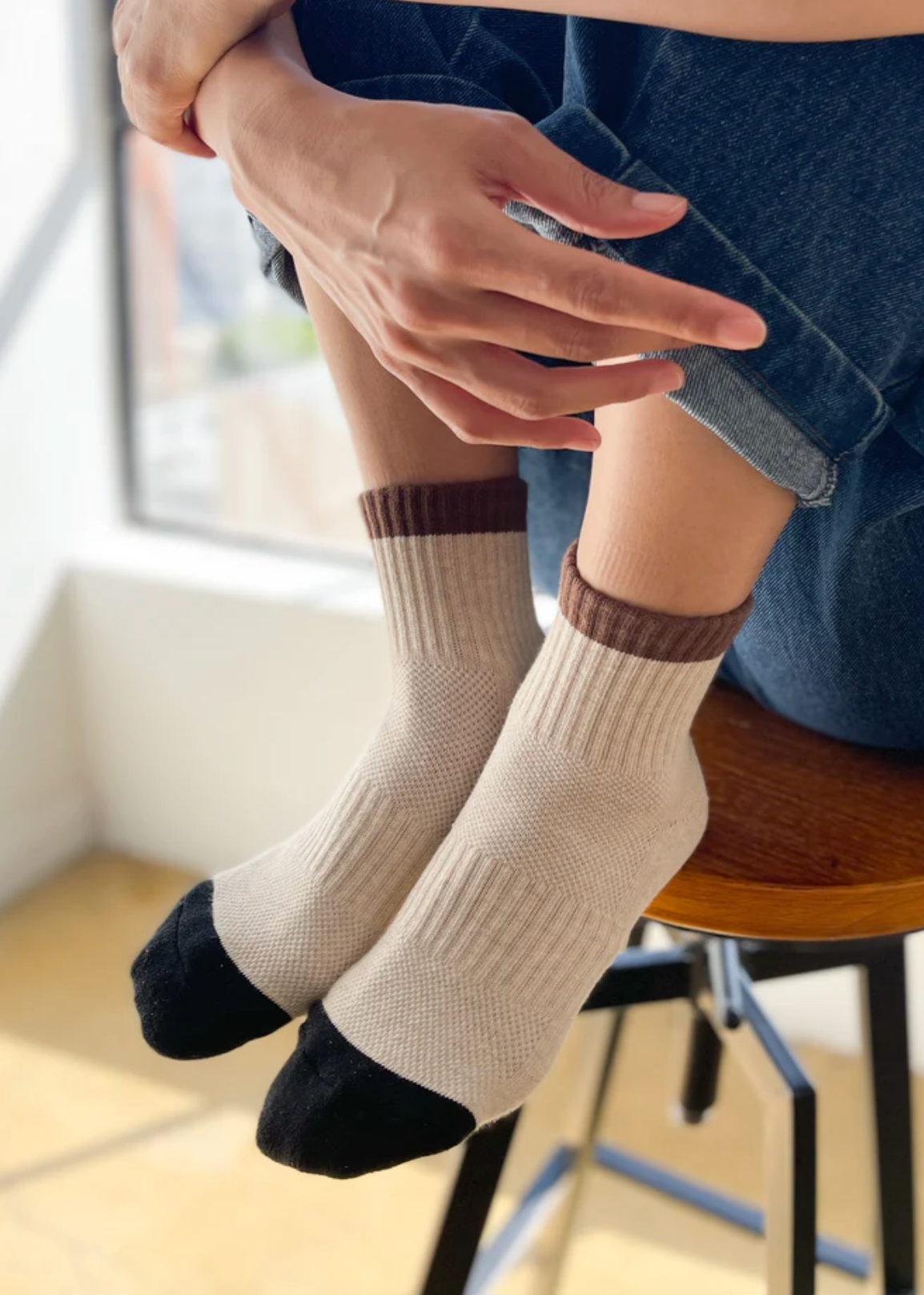 Person wearing beige socks with brown accents sitting on a chair indoors.