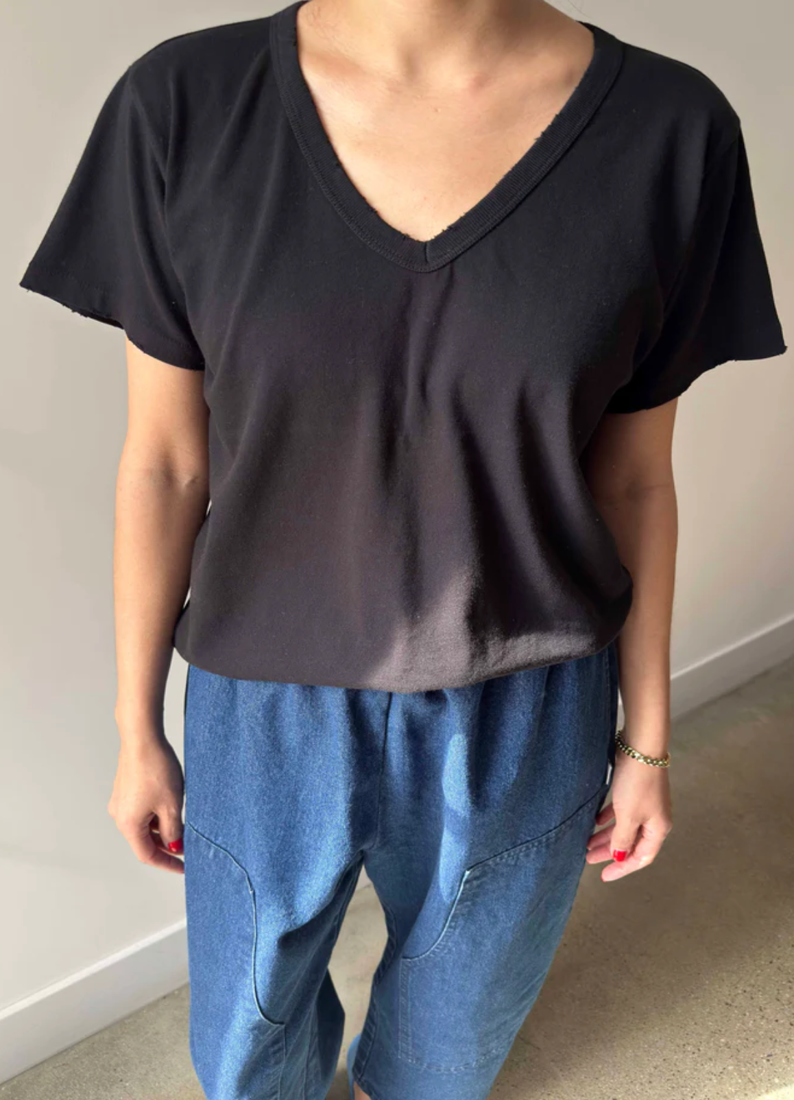 Person wearing a black V-neck t-shirt and blue jeans against a neutral background
