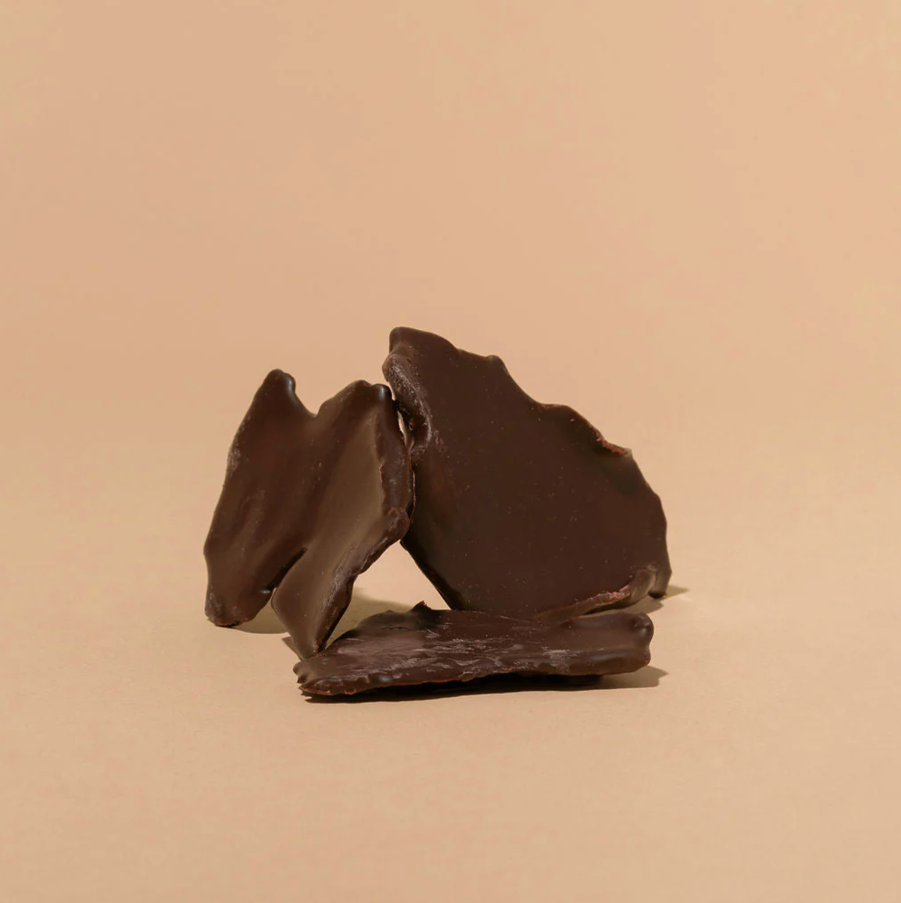 Three dark chocolate covered mangos on a beige background