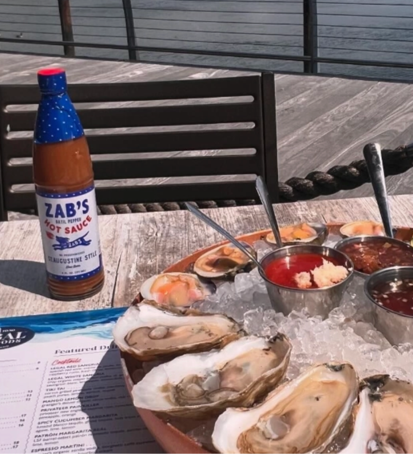 Oysters on a half shell with dipping sauces and a bottle of Zab's hot sauce on a wooden table.