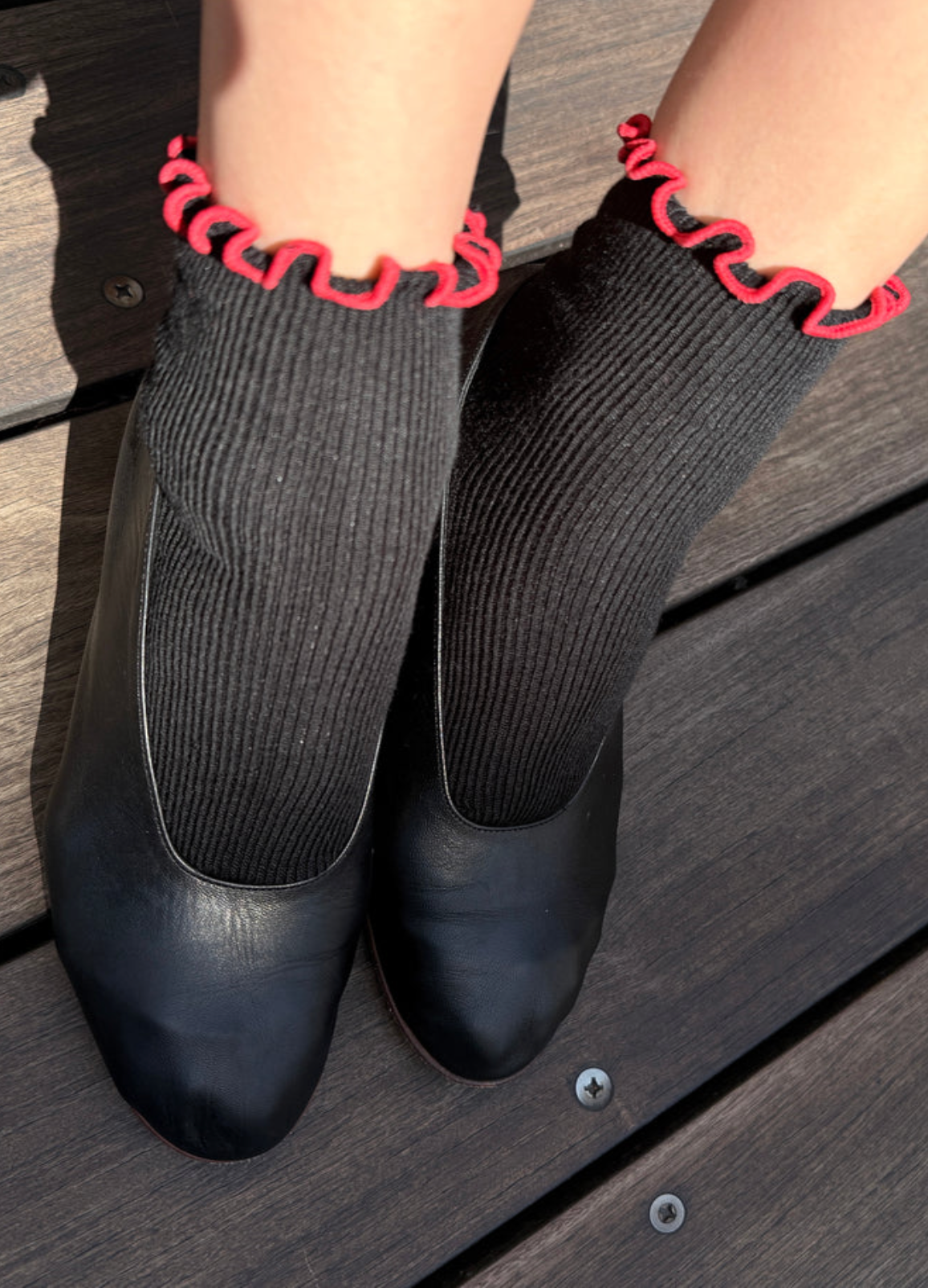 Black shoes with gray socks and red trim on a wooden floor.