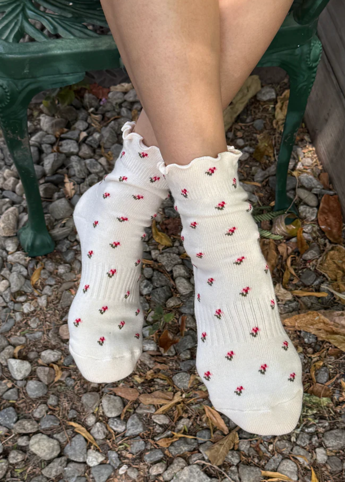 White socks with red patterns worn by a person sitting on a stone ground.