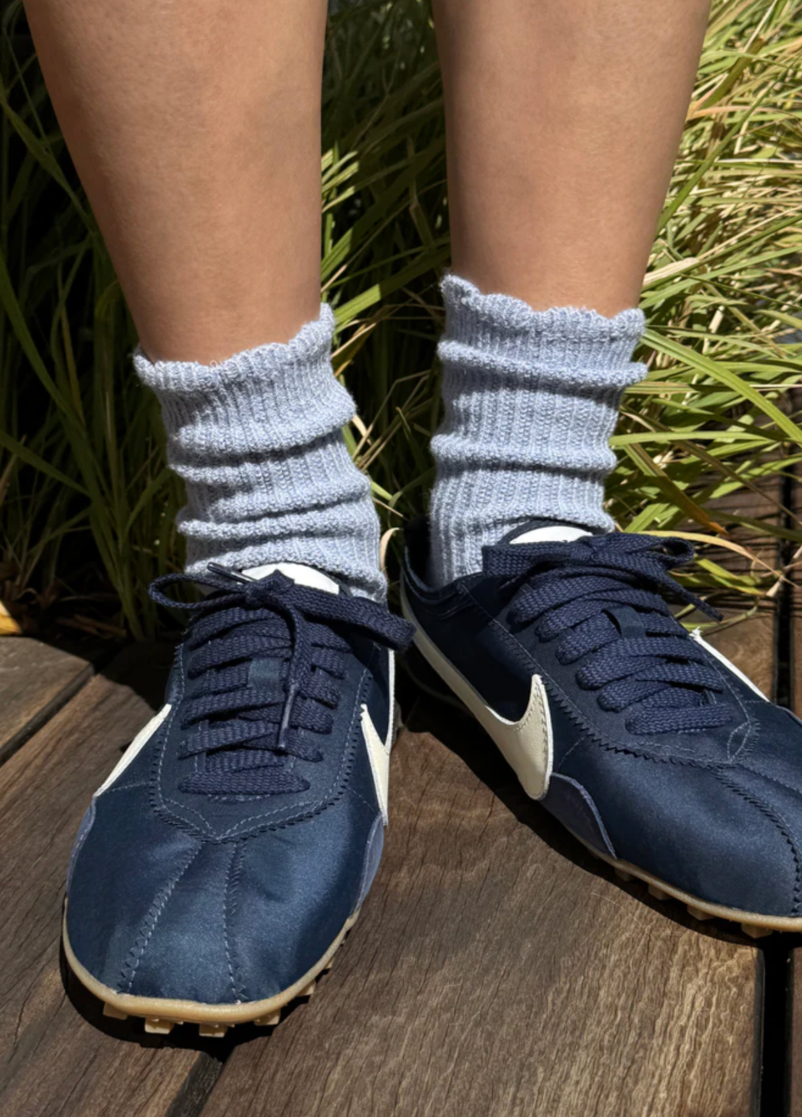 Navy blue sneakers with white soles worn with light gray socks against a grassy background.